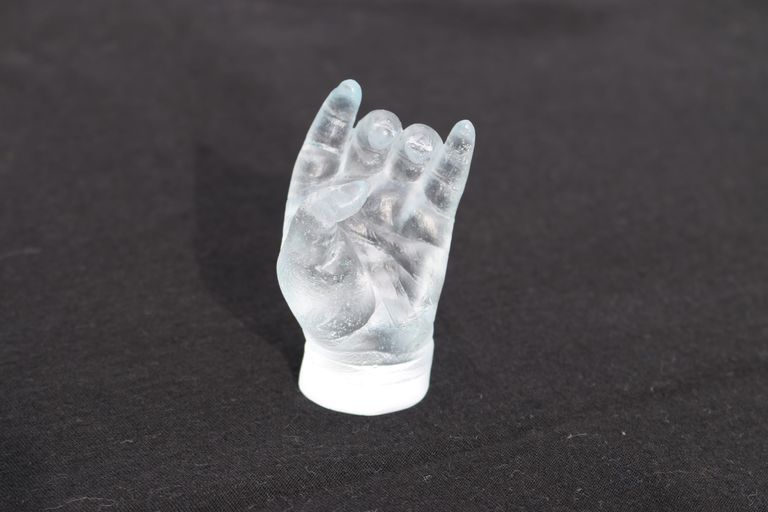 An open baby hand cast in glass with a black background. Light refracted through the glass shows delicate skin detail