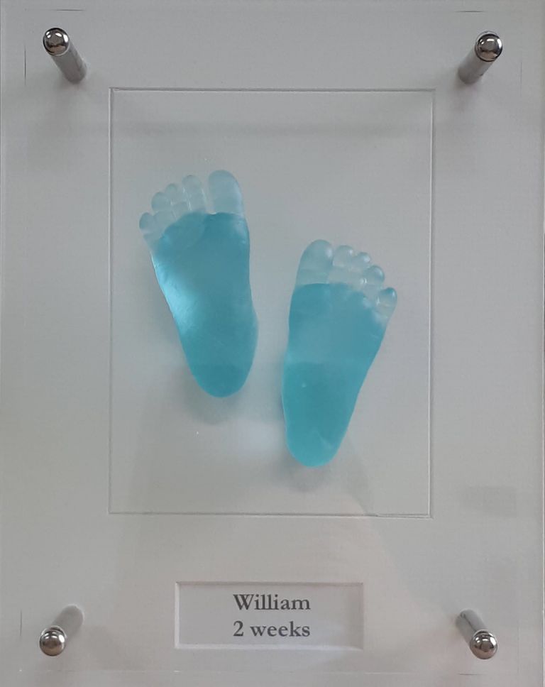 Aqua coloured glass baby feet set in an bespoke acrylic open frame with the baby's name and age displayed below the casts
