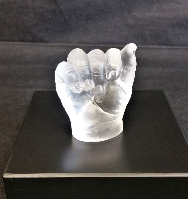 Light reflecting in a glass cast of a baby's gently closed hand placed on a slate base with a black background
