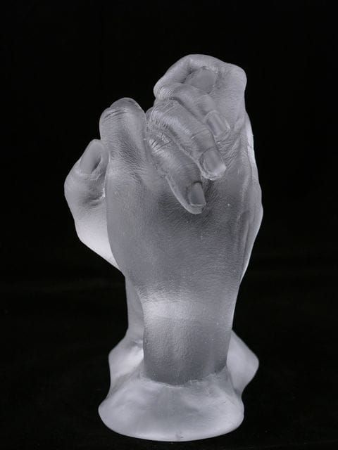 A glass cast of two adults clasping hands stood up on their wrists on a black background