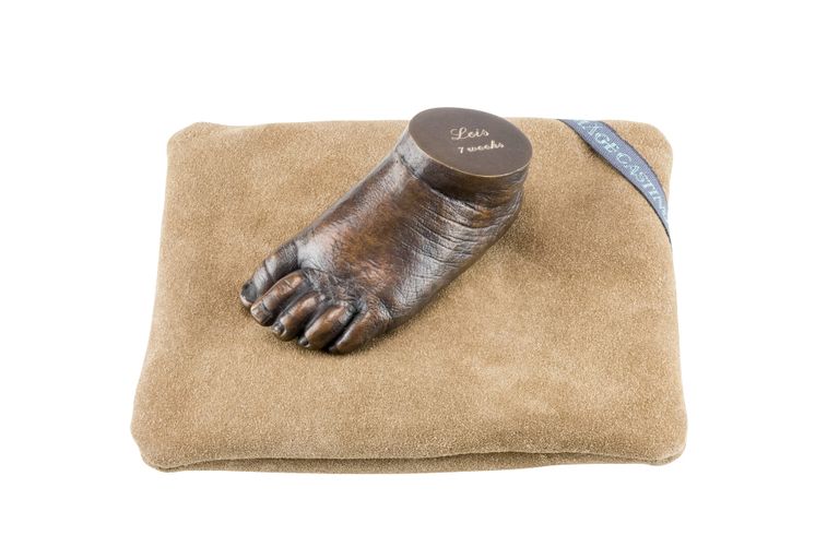A single bronze baby foot engrave on the top sitting on a sand coloured cushion