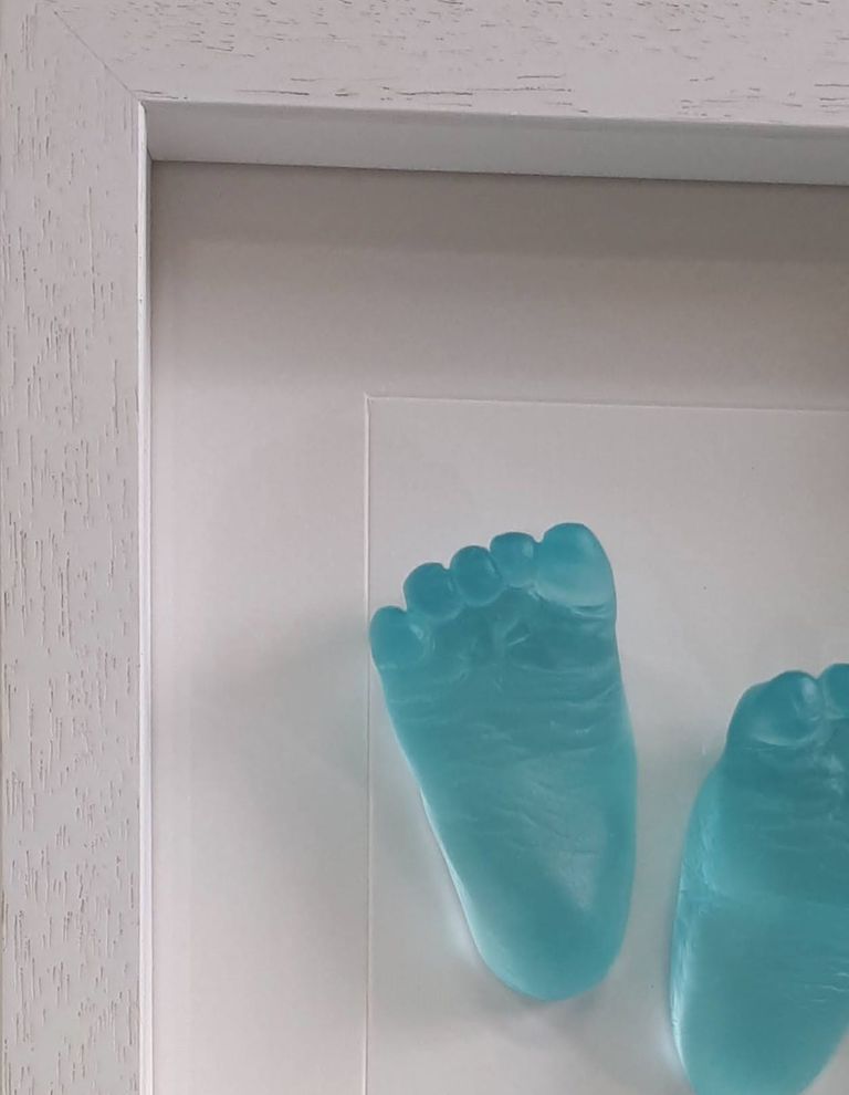 Aqua glass baby foot casts displayed in a white wood effect box frame