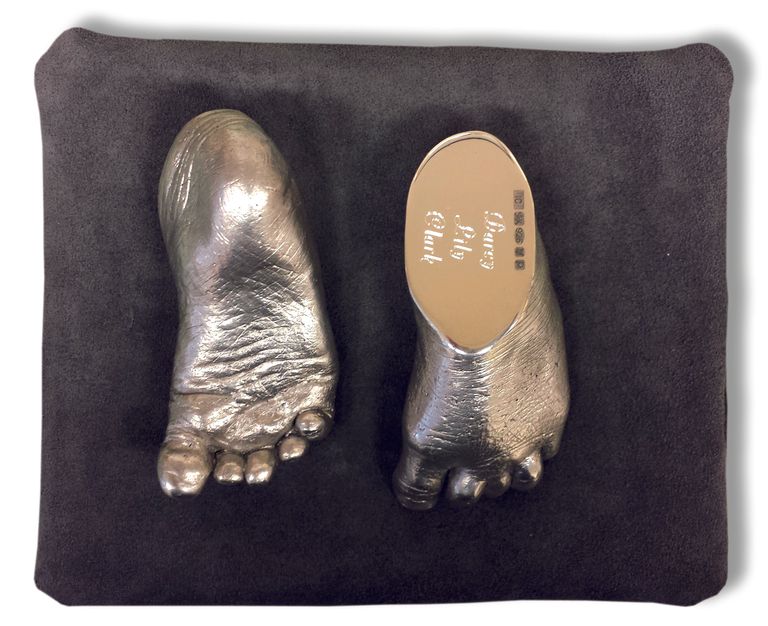 A pair of sterling silver feet showing sole of foot and engraving