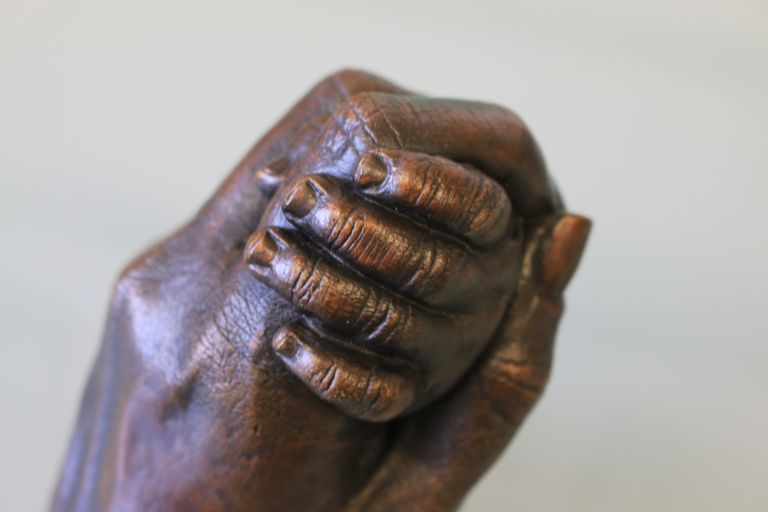 Close up detail of baby's fingers as it clasps dad index finger cast in traditional dark bronze
