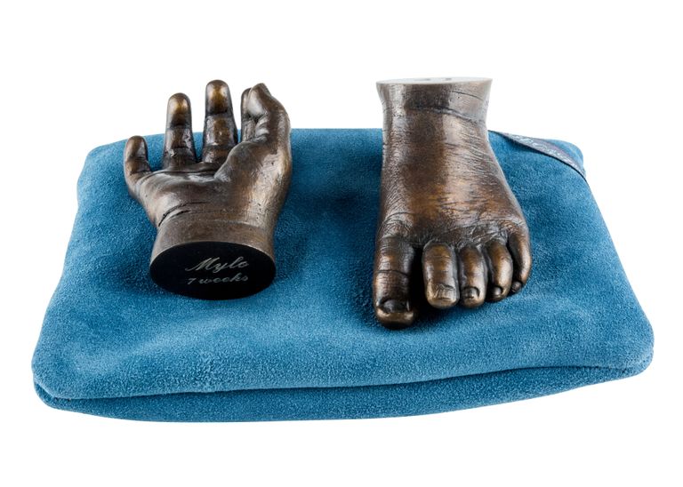 Dark patina bronze baby hand - open and showing the palm - and foot sitting on a teal coloured cushion