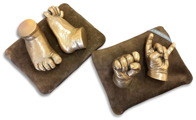 A pair if bronze resin baby feet on a brown cushion set beside the matching hand set
