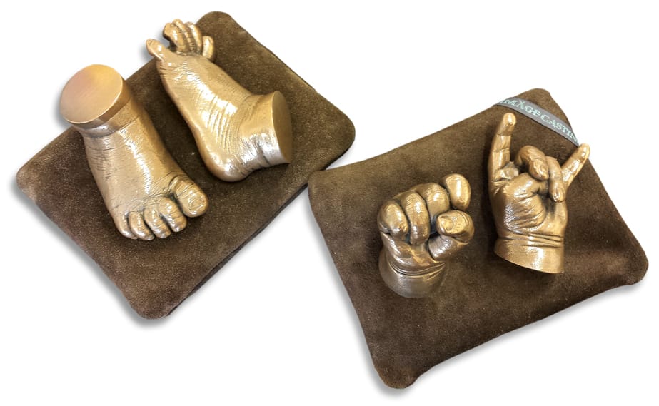 A pair if bronze resin baby feet on a brown cushion set beside the matching hand set
