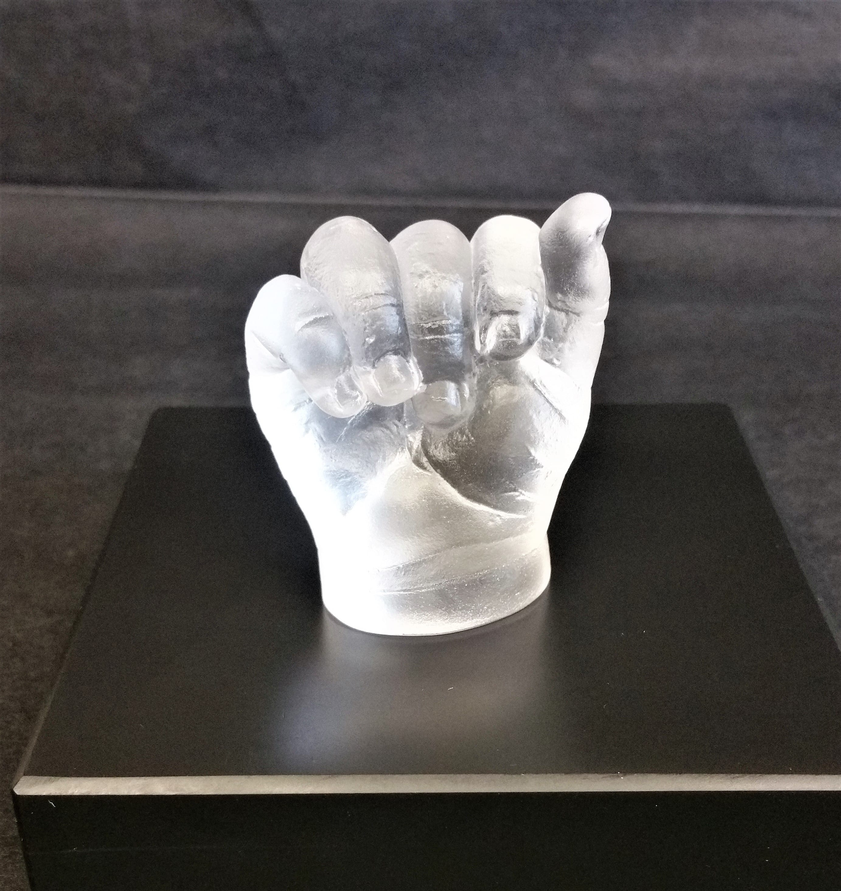 Light reflecting in a glass cast of a baby's gently closed hand placed on a slate base with a black background