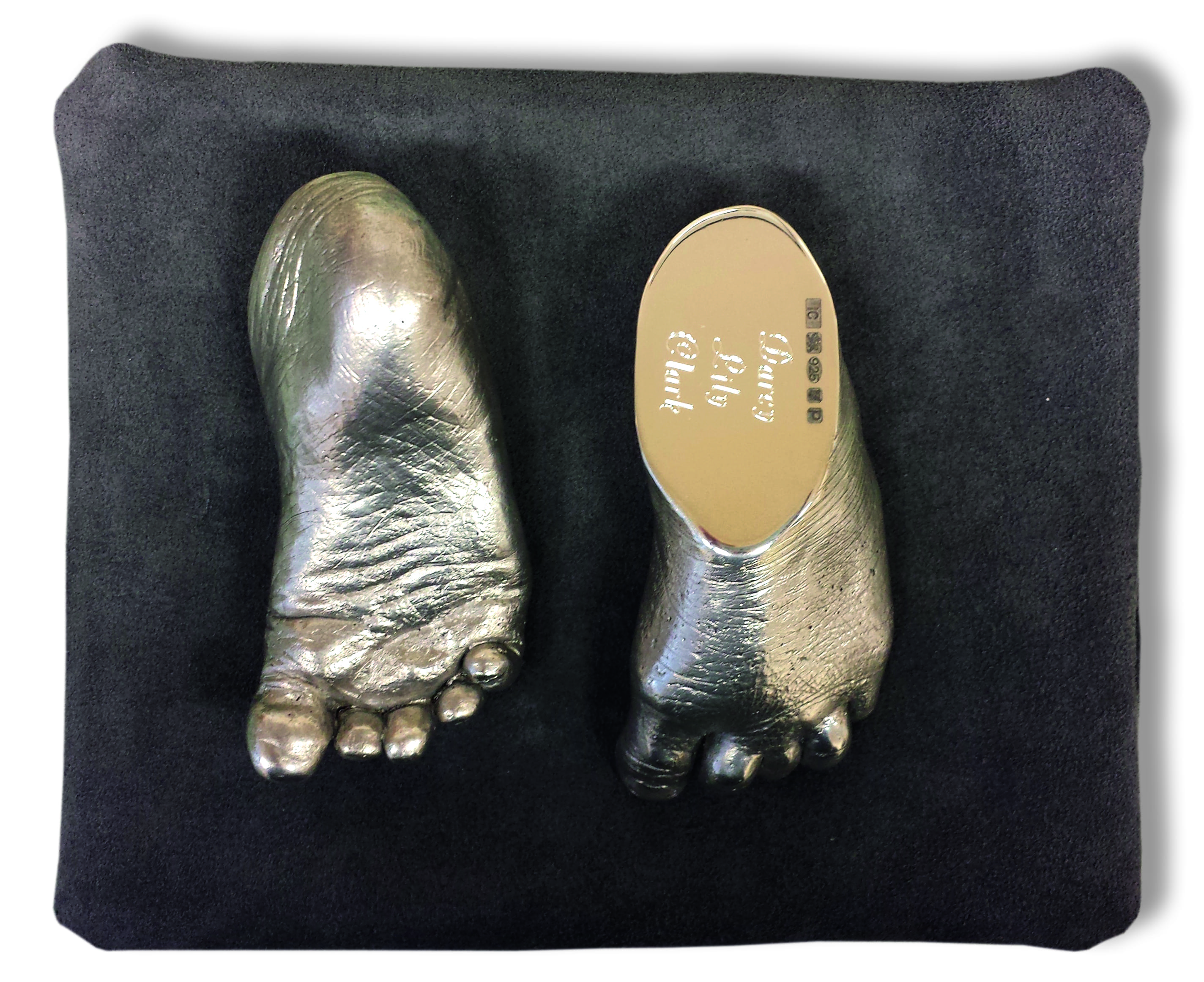 A pair of sterling silver feet showing sole of foot and engraving